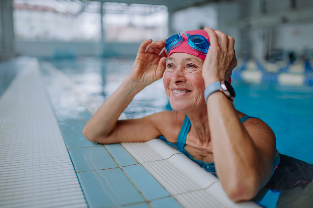 En kvinna med simglasögon lutar sig mot kanten i en inomhuspool.