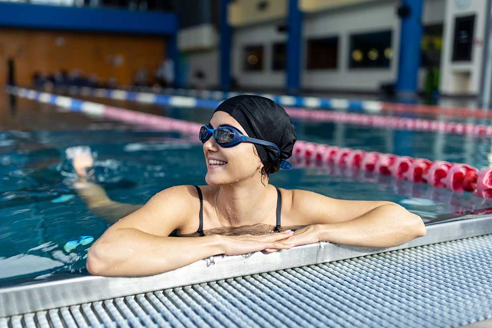 En glad kvinna som vilar mot kanten av en inomhussimbassäng.